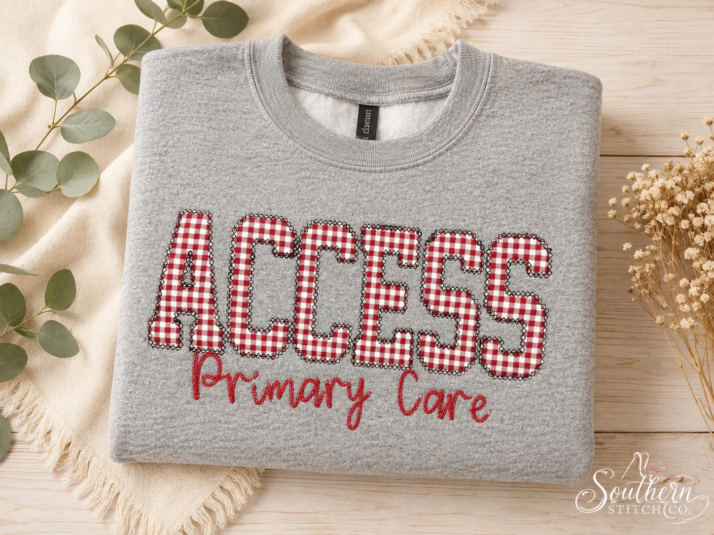 Gray Access Primary Care sweatshirt with red gingham appliqué and red embroidery.